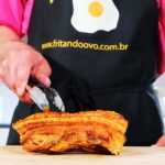 Crispy pork belly on chopping board with chef holding in place.