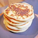 Homemade fluffy pita bread stacked on a wooden board.
