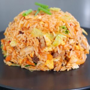 Chinese fried rice with vegetables, pork, and green onions on top served on black plate