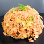 Chinese fried rice with vegetables, pork, and green onions on top in a bowl shape