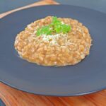 parmesan risotto with fresh parsley on top served on a round black plate.