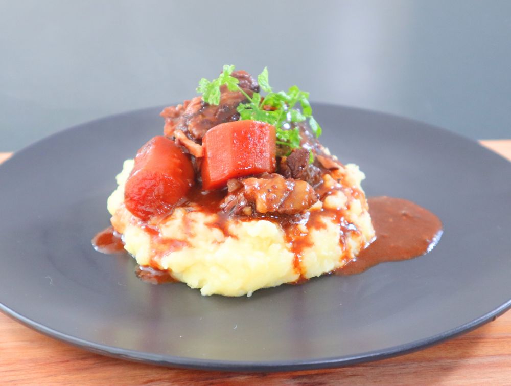 French beef stew Boeuf Bourguignon with carrots, mushrooms, and pearl onions served potato mash on a black plate