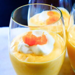 Creamy mango mousse served in a glass topped with fresh mango slices and cream.