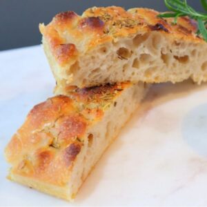 Freshly baked homemade focaccia topped with flaky salt stacked on serving plate