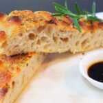 Freshly baked homemade focaccia topped with flaky salt and rosemary in a kitchen setting.