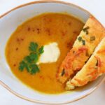 Bowl of creamy leek and carrot soup with harissa, served with crusty bread and cream.