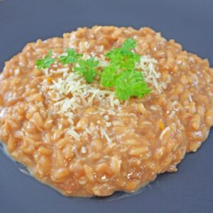 Creamy parmesan risotto served in a black plate with fresh herbs and black pepper
