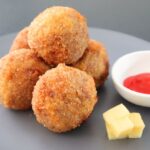 Golden brown arancini stacked served with ketchup and cheese cubes