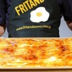 Rustic Italian pizza topped with mozzarella, olives, tomatoes, and fresh basil with man holding tray