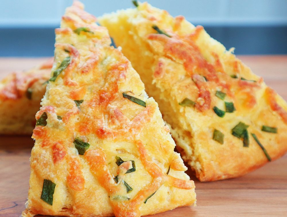 Fluffy homemade cheese bread topped with scallions and mozzarella sliced on a cutting board.
