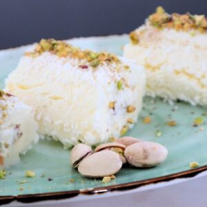 Creamy Turkish milk dessert rolls topped with crushed pistachios and coconut flakes with a side of pistachios on a green plate