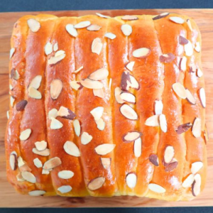 squared shaped bread on wooden serving block sprinkled with almonds